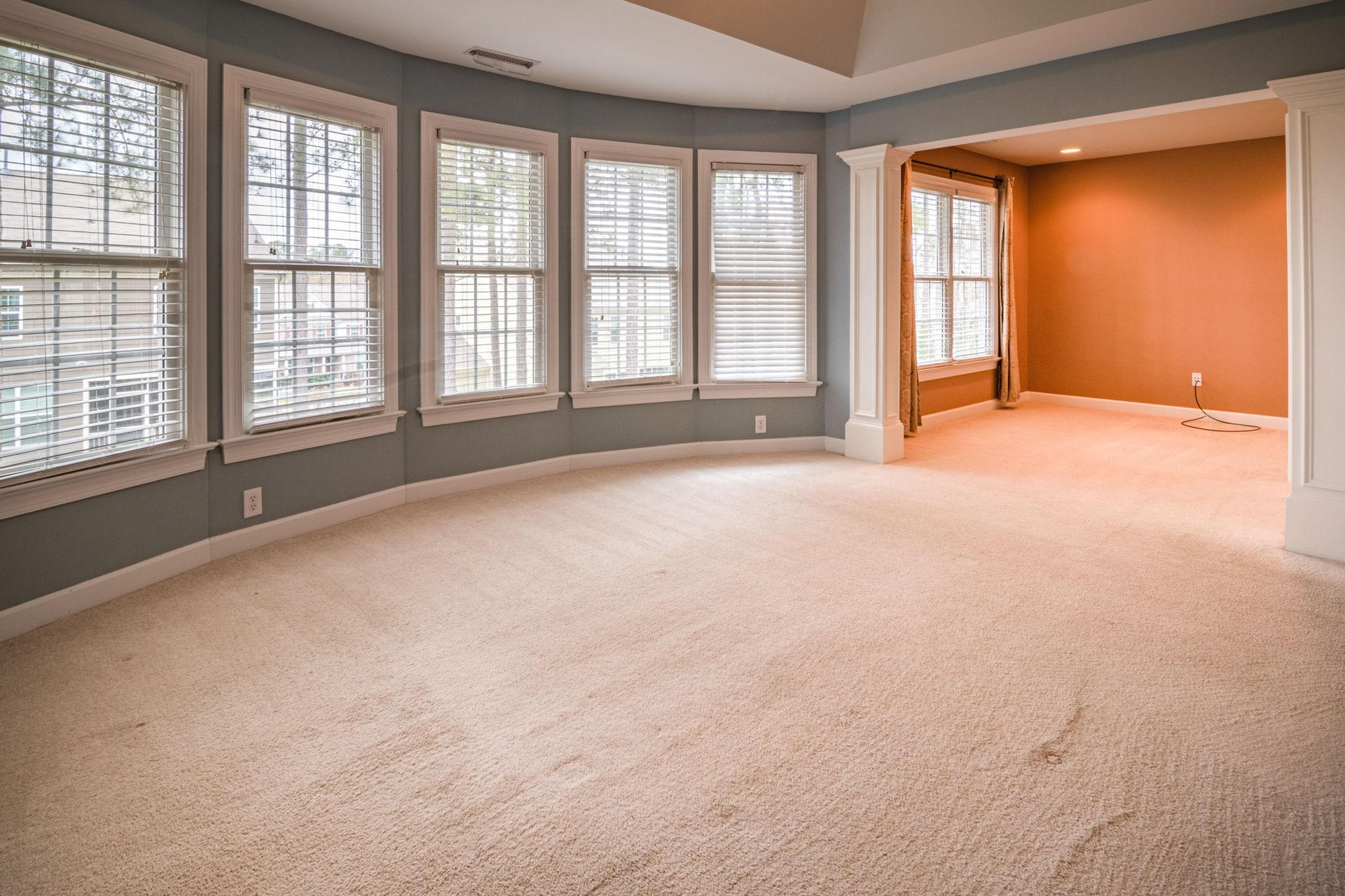 An empty, spacious room with large windows and carpet flooring, ideal for various uses.