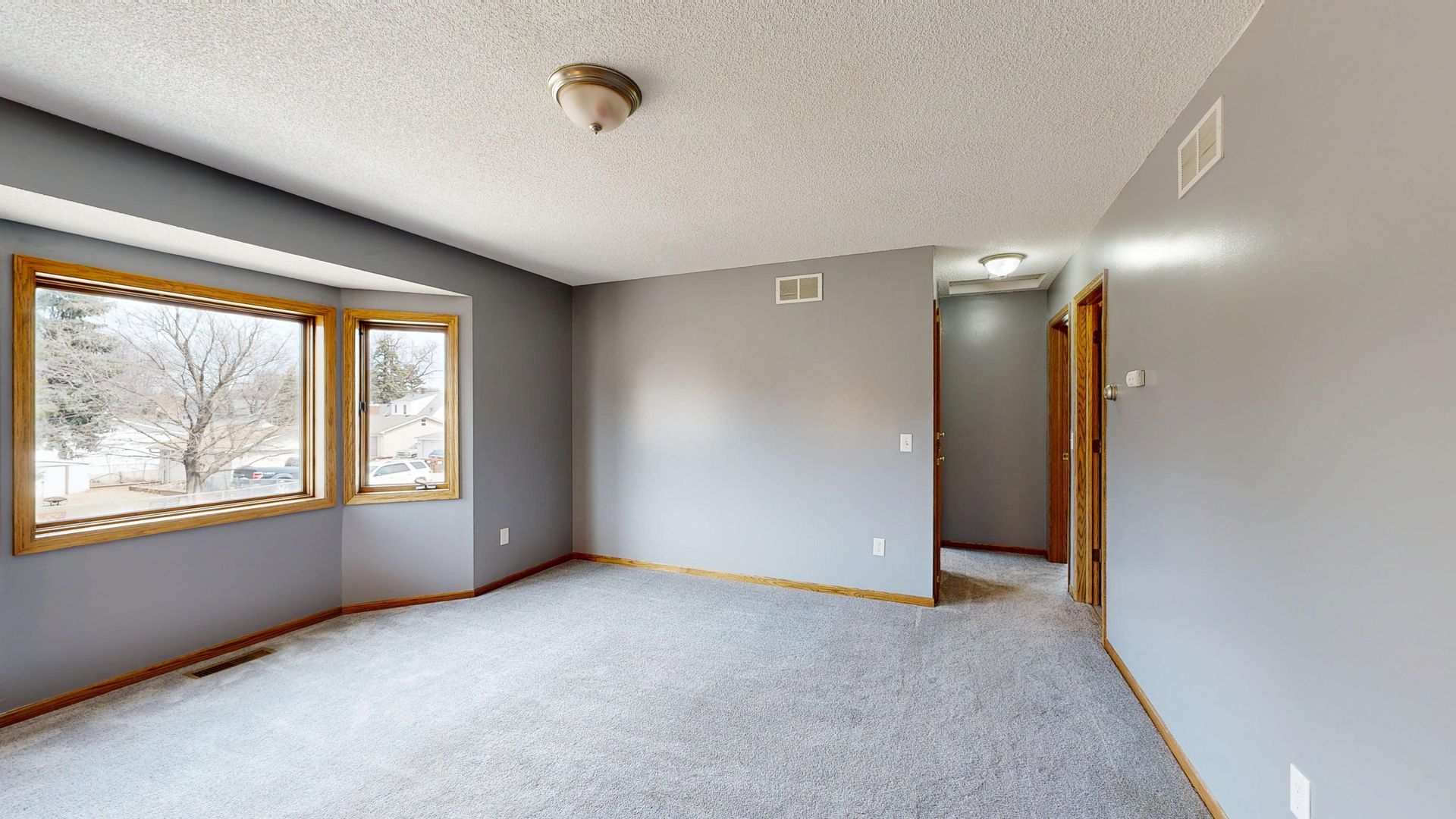 Bright empty room with large windows and grey carpet. Ideal for real estate listings.